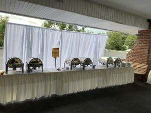 Buffet food warmers on a table for an outdoor graduation party.