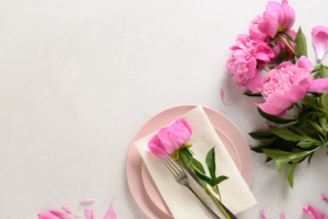 A table setting is pictured. Beautiful pink tulips sit next to the plate and utensils. The tablecloth is white.