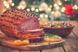A ham on a table with a Christmas tree in the background.